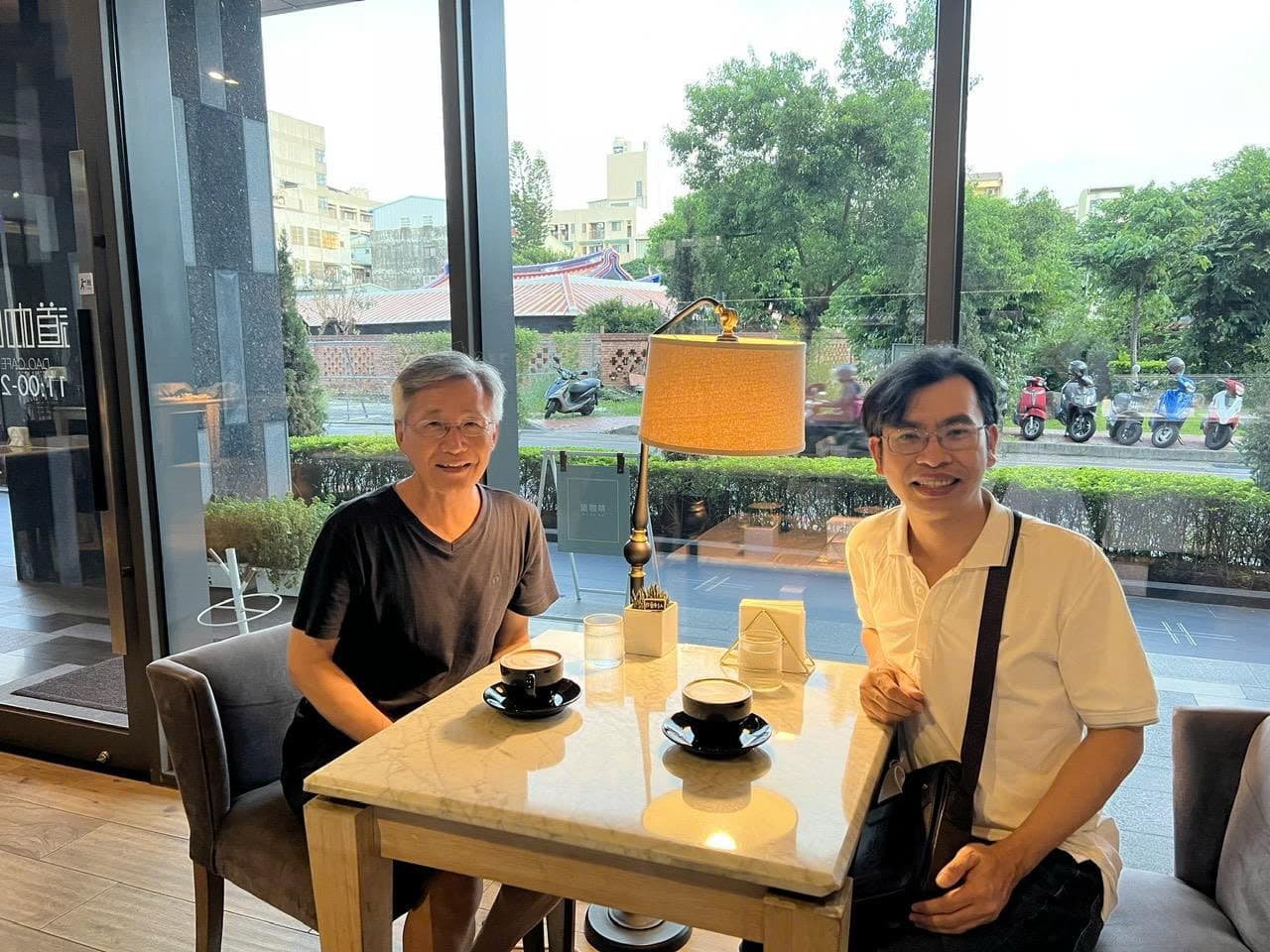 TS. Tam Trinh (bên phải) và GS. Chi-Chur Chao ngồi trò chuyện bên bàn cà phê cạnh cửa kính
